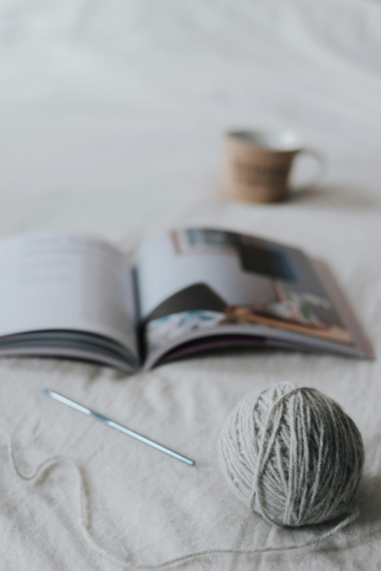 Yarn ball and needle placed on bed near opened magazine