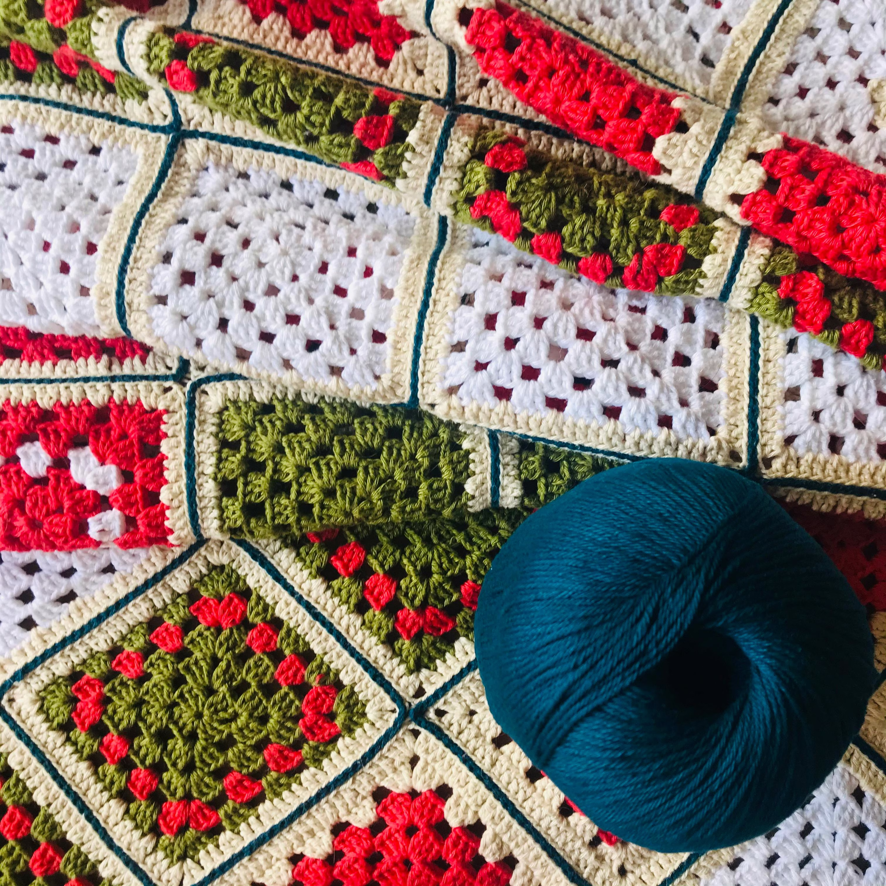 Blue yarn skein on top of a multi colored granny square blanket that has red, white, green and tan.