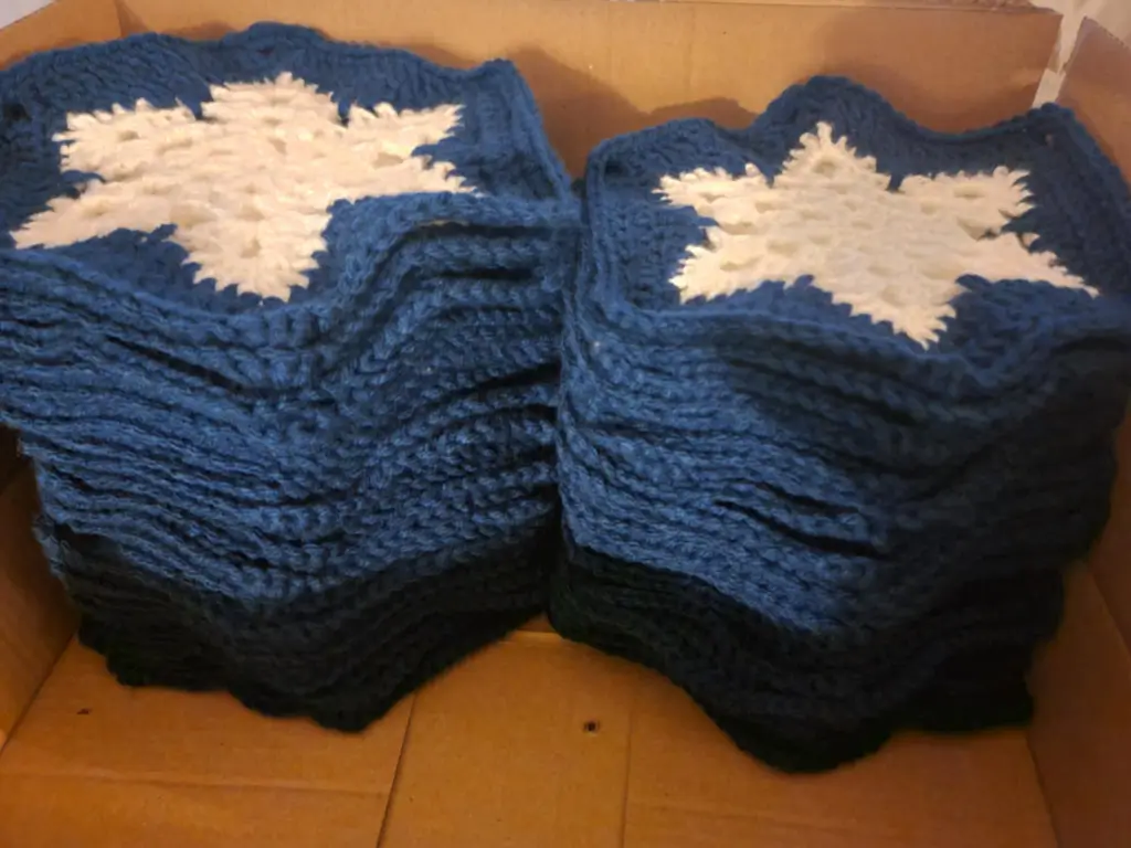 Picture of individual blue and white granny squares that have a snowflake pattern in two piles
