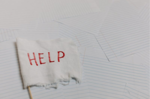 Picture of single sheets of lined paper spread messily across a flat surface with a white flag that has the word HELP written in red letters