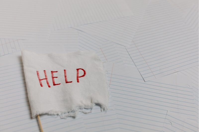 Picture of single sheets of lined paper spread messily across a flat surface with a white flag that has the word HELP written in red letters