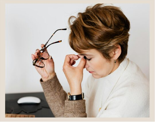 Picture of a side profile of a woman holding her glasses and pinching the bridge of her nose to indicate stress or burnout
