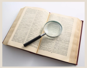Picture of a white background with an open dictionary that has a magnifying glass laying on top of it.